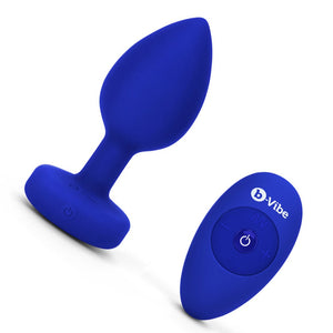 The b-Vibe Vibrating Jewel Butt Plug is shown against a blank background next to its 4 buttoned remote. The plug is a size L/XL, which is Blue Sapphire colored.