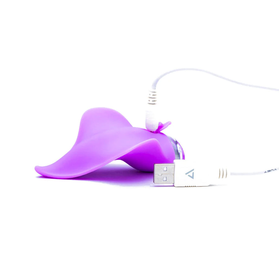 The Clandestine Mimic Massager External Vibrator in Lilac is shown against a blank background. The toy is shown with it’s USB charger plugged into it.
