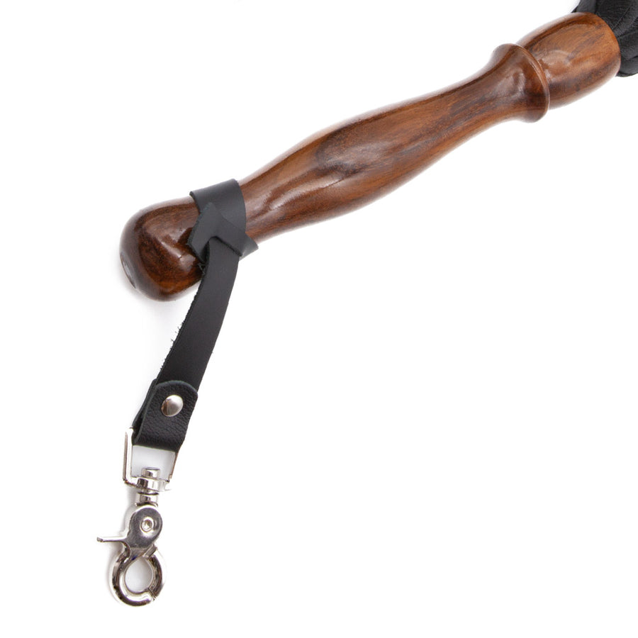 A close up image of the Sissoo Rosewood Long Handle Leather Flogger on a white background. Shown is the included leather hanger strap with crab-claw hook attached to the handle of the flogger.