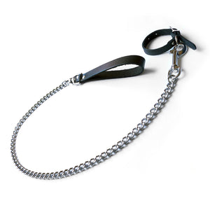 The Buckling Cock Ring And Chain Leash Set is shown against a blank background. The cock ring is made of black leather, as is the leash handle. The chain on the leash and the hardware on the cock ring are silver.