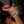 Load image into Gallery viewer, A close-up of a woman&#39;s hand with red painted nails is shown. She wears the Deluxe Padded Medical Leather BDSM Wrist Restraints. The cuffs are made of a wide piece of tan leather with a white border. They have a large D-ring and are padlocked.
