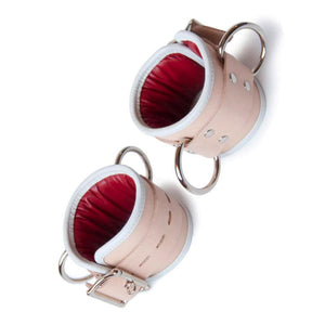 The Deluxe Padded Medical Leather BDSM Wrist Restraints are shown against a blank background. The cuffs are made of tan leather with a white border and a red inner lining. They have metal hardware.