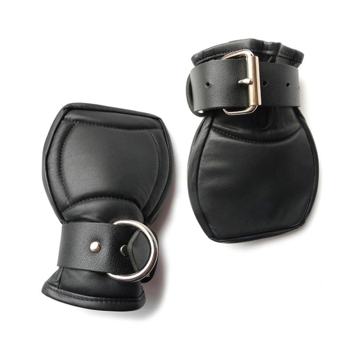 The Deluxe Padded Leather Fist Mitts are shown against a blank background. The mitts are smooth on top and are made of black leather with silver hardware. There are adjustable buckling straps with a D-ring around the wrists.