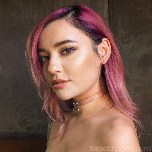 A close-up of a shirtless pink-haired woman is shown wearing the Clear CTRL Vinyl Choker. The collar is a thin band of transparent PVC with a small, dangling O-ring in the center.