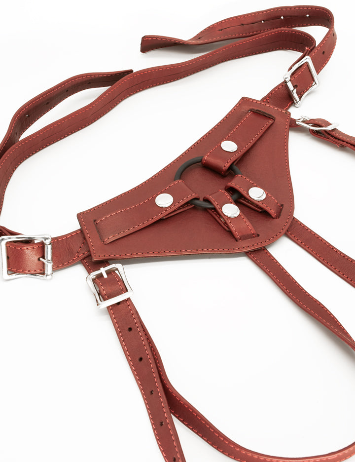 The Full Curves Leather Strap-on Harness in wine is displayed against a blank background. The leather is reddish brown. There is a black silicone O-ring in the center held in place by snap closures.