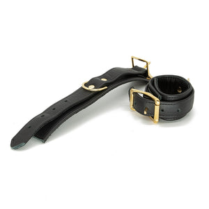 A pair of black Garment Leather Wrist Cuffs With Brass Gold Hardware are shown against a blank background. One of the cuffs is buckled and one is laying flat.