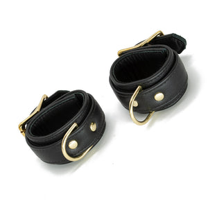 A pair of black Garment Leather Wrist Cuffs With Brass Gold Hardware are shown buckled against a blank background.
