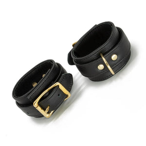 A pair of black Garment Leather Ankle Cuffs With Brass Gold Hardware are shown buckled against a blank background.
