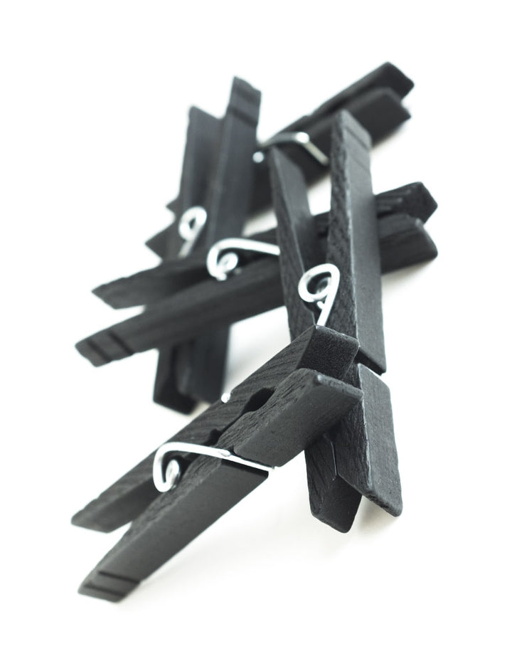 Five black clothespins from the Gripper Clothespins 30 Pack are displayed against a blank background, piled on top of each other.