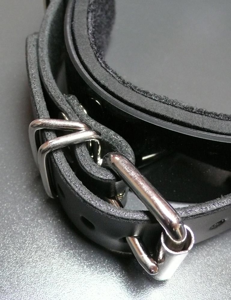 A close-up of the buckling strap of the Half Moon Bit Gag By Scott Paul Designs is shown on a grey table.