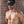 Load image into Gallery viewer, A shirtless, muscular brunette man with light facial hair poses next to a brick wall, wearing the black Mistress Heather Leather Blindfold.
