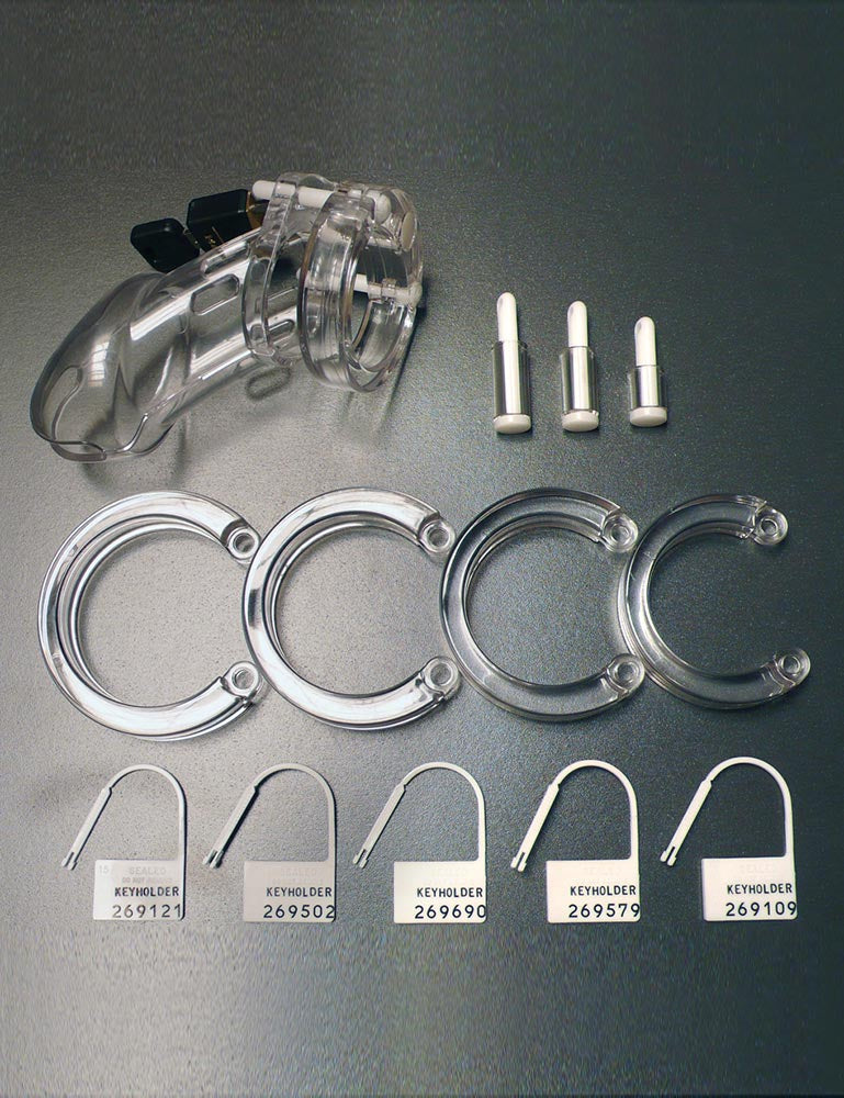  The contents of the CB-6000 Package Male Chastity Kit are shown against a silver background. Displayed are the assembled cage with a brass padlock attached, 4 different-sized rings, 3 additional spacers and locking pins, and 5 plastic locks.