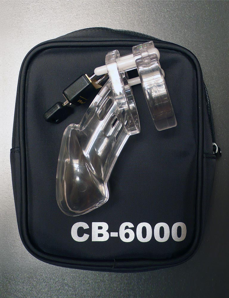 The assembled chastity cage is shown resting on top of the CB-6000 Package Male Chastity Kit case. The zipper case is made of black fabric with “CB-6000” in white on the bottom. 