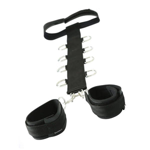 The black nylon Neck And Wrist Restraints are shown against a blank background. The restraint consists of a long vertical black nylon strap with a row of metal D-rings on either side. At the top of the strap is a collar, and at the bottom are wrist cuffs.