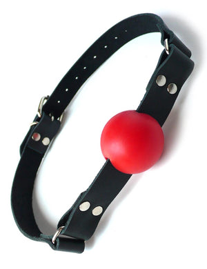 The red rubber ball gag is displayed against a blank background. It is a matte red rubber ball attached to a black leather strap with silver hardware, which buckles behind the head.
