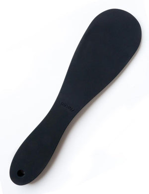 The Tantus Pelt Paddle, a matte black silicone rounded paddle with a curved handle, is displayed against a blank background.