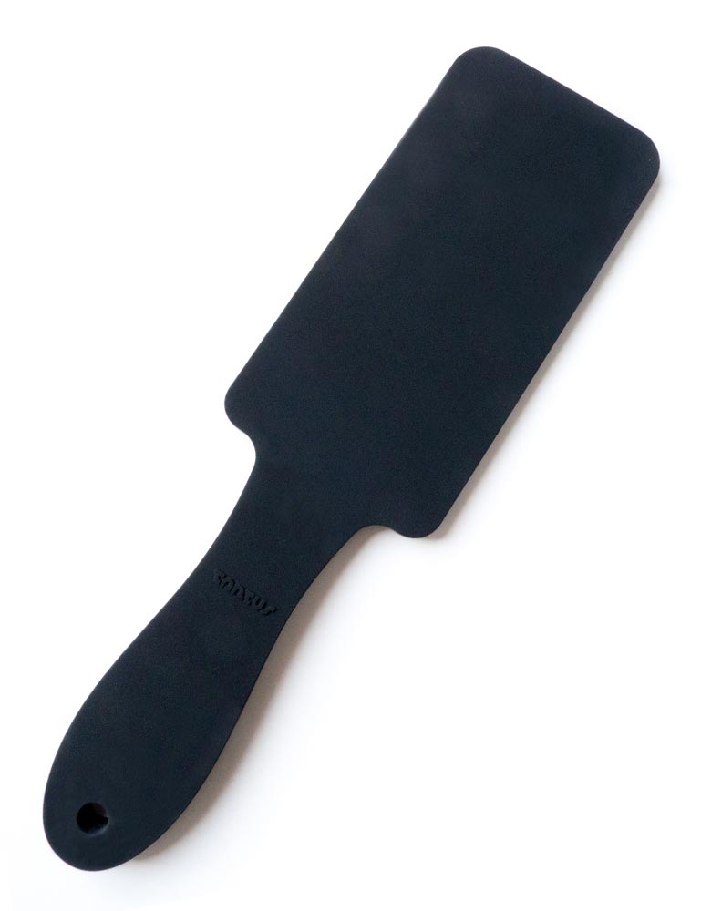 The Tantus Thwack Paddle is displayed against a blank background. The paddle is rectangular with a rounded handle and is made of black silicone.