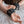Load image into Gallery viewer, A close-up of a woman’s hands is shown. She is lying on a white bed, and her hands rest above her head. She is wearing the Silicone Bondage Locking Wrist Cuffs, which are attached to each other via a metal snap hook.
