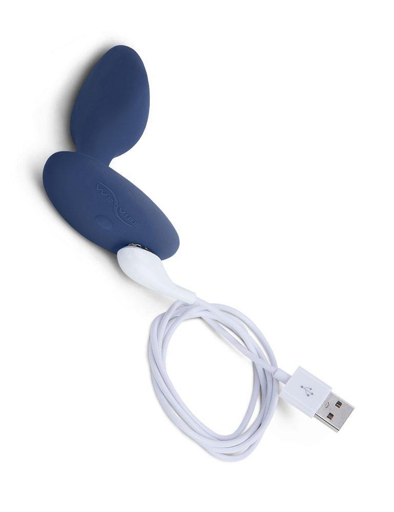 The We-Vibe Ditto Vibrating Butt Plug is displayed against a blank background. The plug’s white USB charger is attached to its magnetic charging ports.
