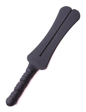 The Tantus Trip 2 Tawse Silicone Paddle is displayed against a blank background. It is made of matte black silicone. The handle is rounded and textured with a small hole at the bottom.