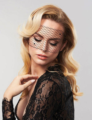 A blonde woman in a black lace top poses in front of a grey background with her eyes closed. She wears the Louise Decal Mask, which is a black lace blindfold-shaped mask.