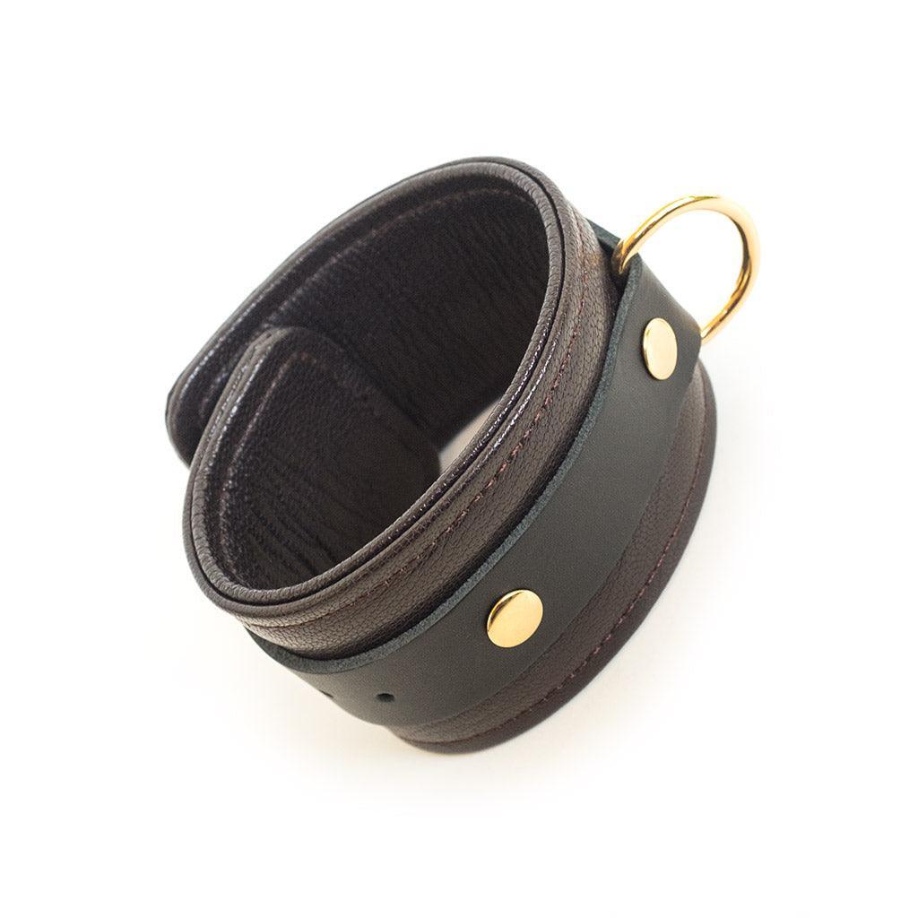 One of the Brown Leather Ankle Restraints With Gold Accent Hardware is shown against a blank background, displaying the cuff’s D-ring.