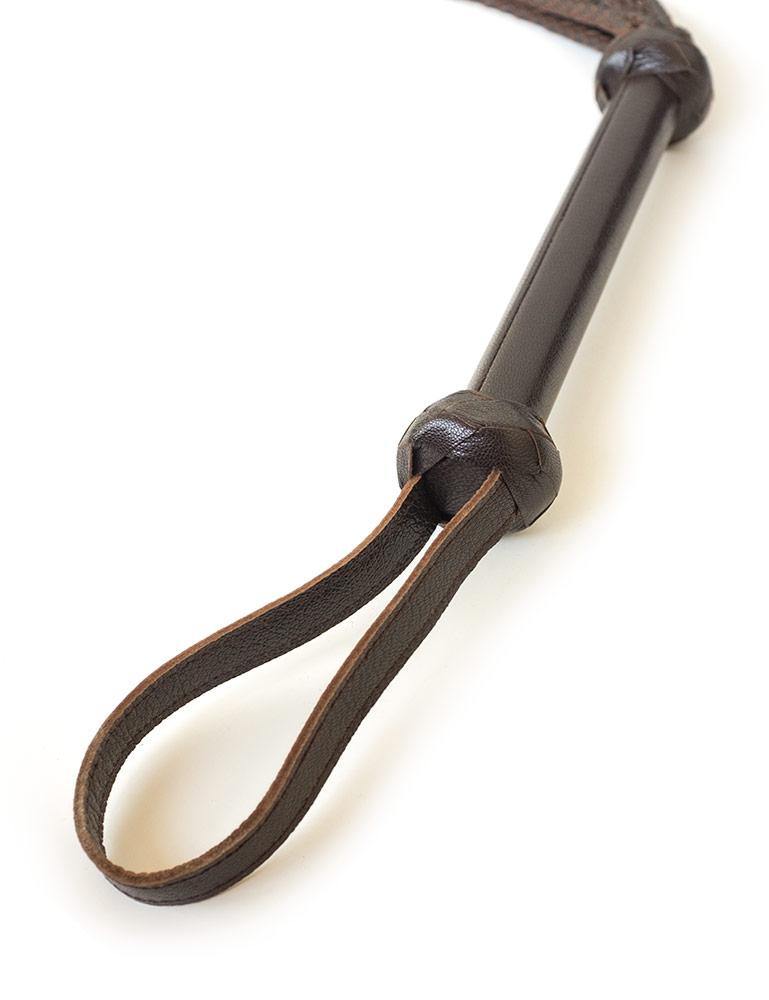 A close-up of the handle of the Brown Leather Braided Whip is displayed against a blank background. The handle widens slightly at the top and the end, where it is surrounded by braided brown leather pieces.