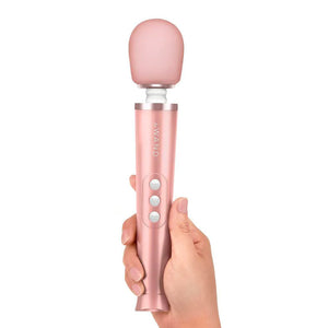 A hand is shown holding a Le Wand Petite Rechargeable Vibrating Massager in Rose Gold against a blank background.