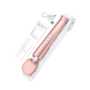 A Rose Gold Le Wand Petite Rechargeable Vibrating Massager is shown with the contents of the package against a blank background. The image displays the wand, the manual, a zip-up case, and charging cable.