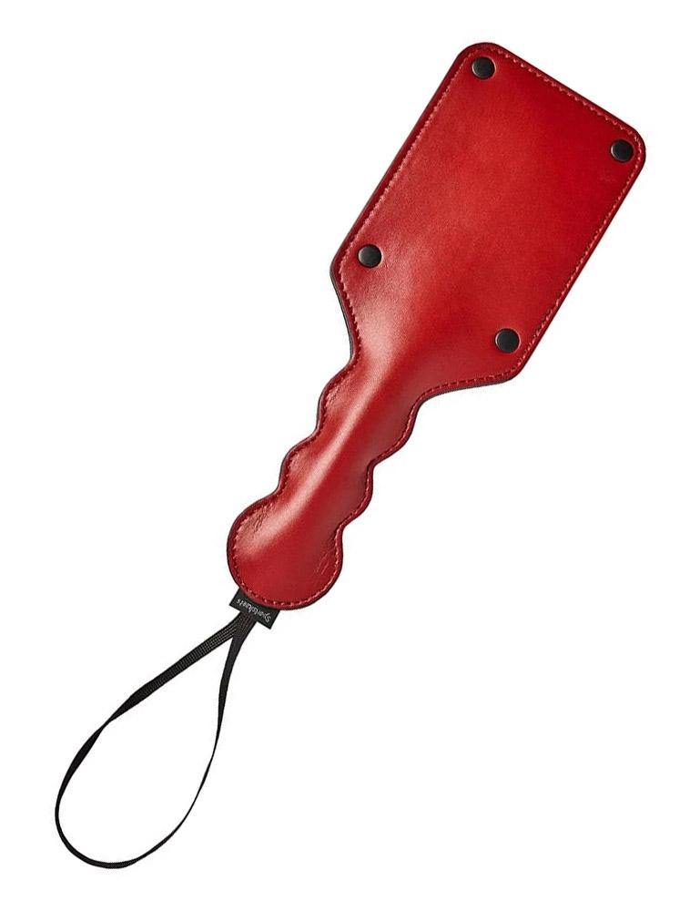 The Saffron Square paddle, made of red faux leather, is displayed against a blank background. The paddle is rectangular with rounded edges, and the handle has a bubble design with a wrist loop at the end.