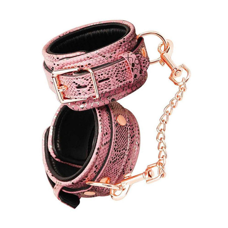 A pair of Rose Gold Snake Ankle Cuffs are shown against a blank background. The cuffs have a pink snakeskin design and rose gold hardware, including a lockable buckle, D-rings, and an included chain with claw hooks at the ends.