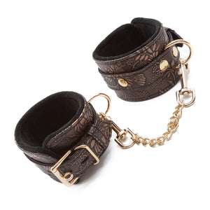 A pair of Vegan Floral Wrist Cuffs With Faux Fur are displayed against a blank background. The cuffs have an ornate floral pattern and gold hardware, including a lockable buckle, D-ring, and an included chain with claw hook ends.