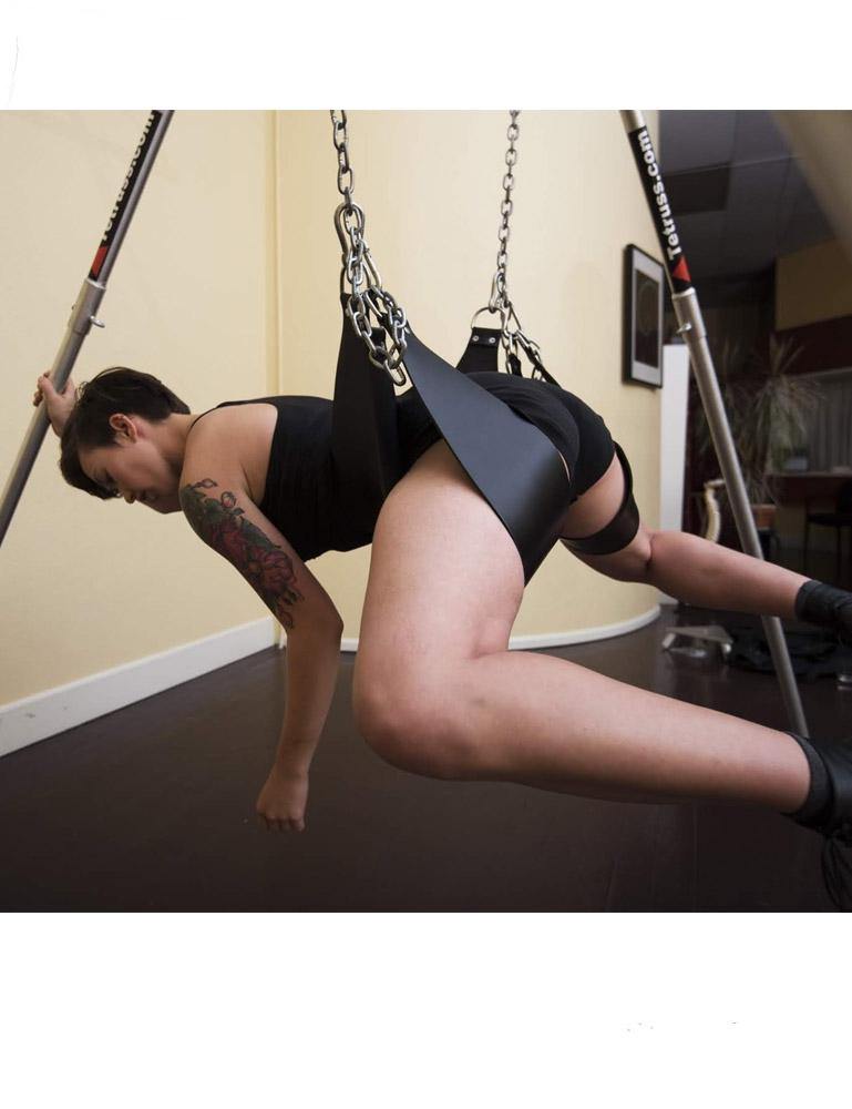 A woman is shown from the side using the Tetruss Portable Dungeon Deluxe Bundle. She is lying face down with her torso supported by one stirrup and her legs supported by the two others. She is grabbing one of the poles of the frame.