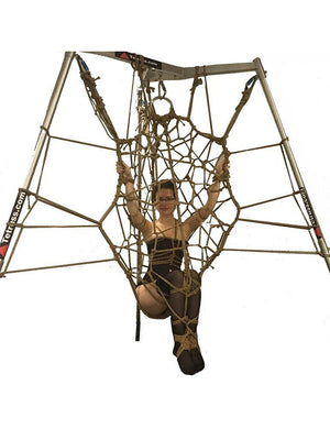 The Tetruss Maxximus Suspension Bondage Frame is shown in use against a blank background. The frame is silver and has 3 poles arranged triangularly, which are connected at the top. A woman is shown tied up in a rope web attached to the frame.