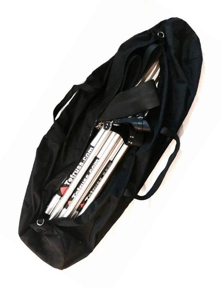 The Tetruss Travel Bag is shown against a blank background. It is a black, cylindrical canvas bag with black straps. It is unzipped and is shown with a Tetruss bondage frame, leather stirrups, and suspension cuffs inside of it.
