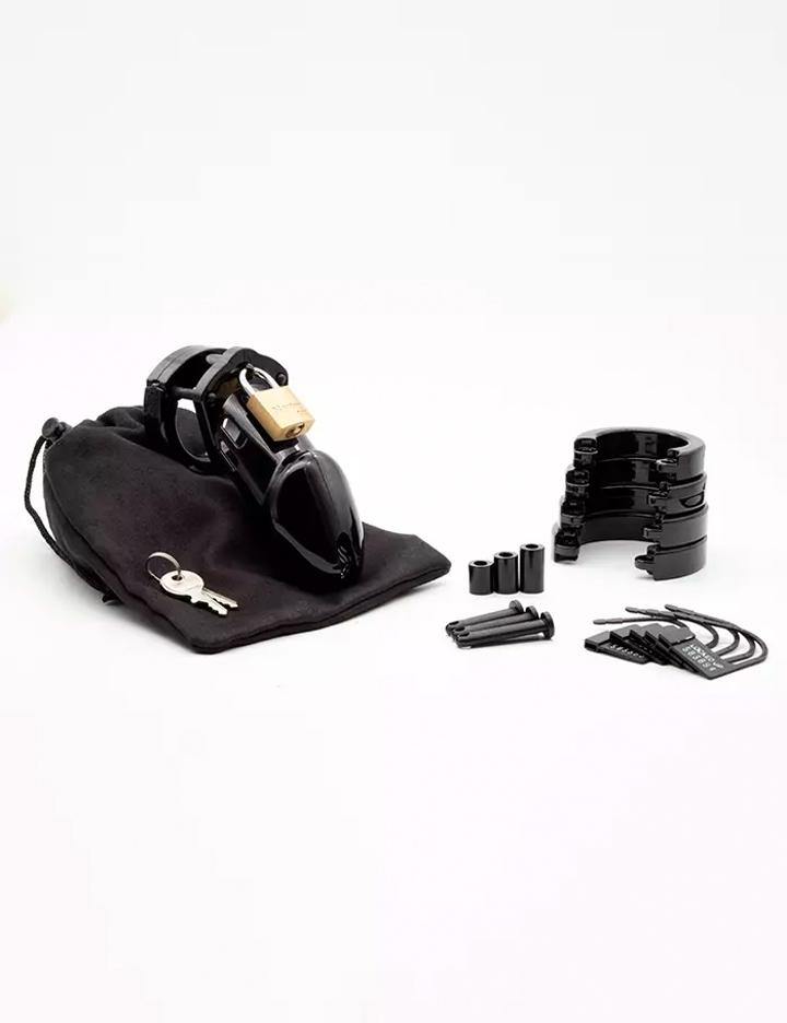 The contents of the CB-6000 Male Chastity Device in black are shown against a blank background. Displayed are the cage with the padlock, a black cloth storage bag, 5 different sized rings, 4 locking pins and 4 spacers, and 5 labeled plastic locks.
