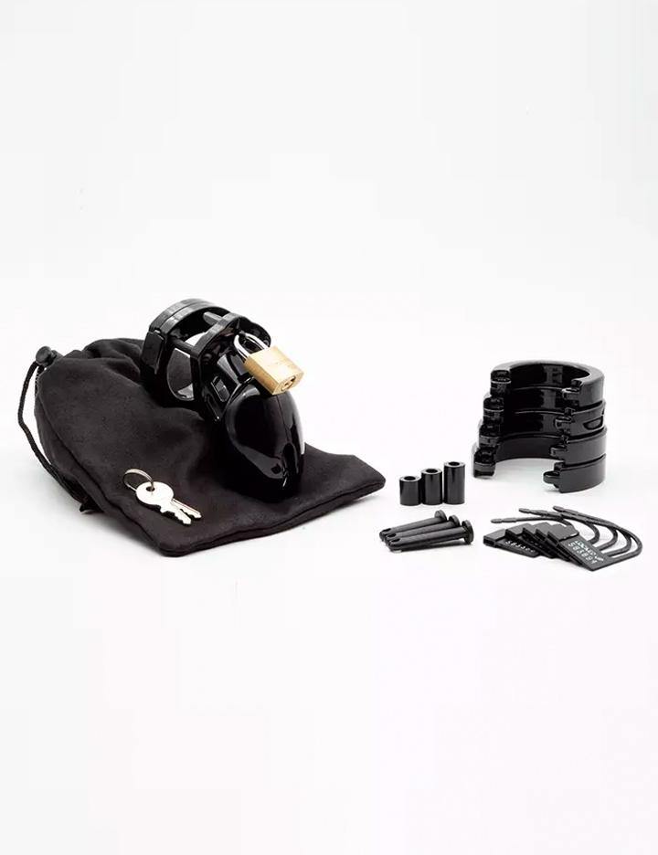 The contents of the CB-6000S Male Chastity Device in black are shown against a blank background. Displayed are the cage with the padlock, keys, a black cloth storage bag, 5 different sized rings, 4 locking pins and 4 spacers, and 5 labeled plastic locks.