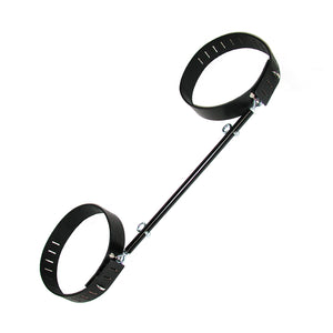 The black Thigh Spreader Bar is shown against a blank background. It is made of a black rod with two metal eye holes facing outwards. On each end of the bar, there are adjustable black leather thigh cuffs with hasp closures.
