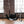 Load image into Gallery viewer, The black Leather Sling with metal rivets is suspended from the ceiling by chains in a brick room. It has a large central piece and two smaller leather pieces for suspension on top and bottom. Stirrups hang from the chains at the bottom of the swing.
