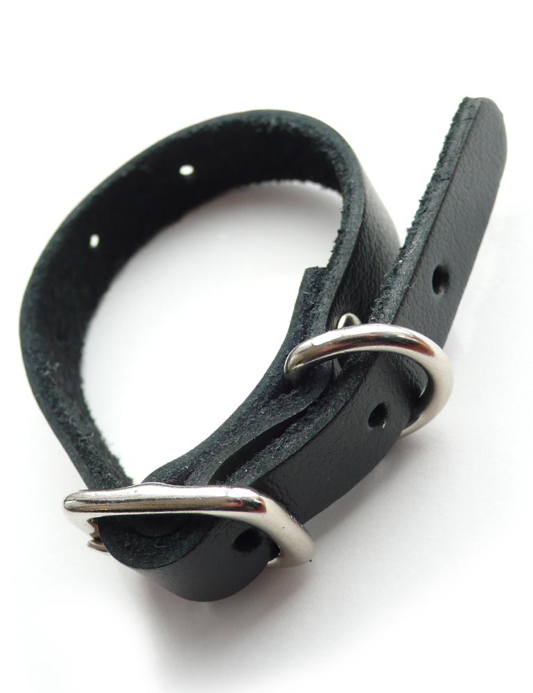 The black leather Buckling Cock Ring with D-Ring is displayed against a blank background. It is a small notched strip of black leather with a silver metal buckle closure and a small D-ring near the buckle.