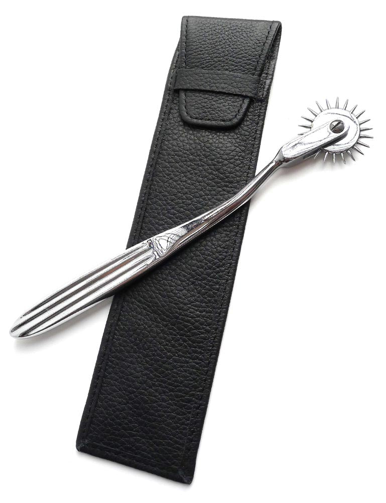 The KinkLab Wartenberg Pinwheel with Leather Sheath is displayed against a blank background. The pinwheel is made of silver metal with a single row of spikes. It rests on top of the case, made of black leather.