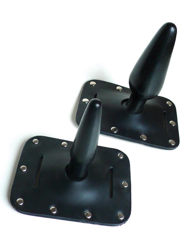 Two Harness Butt Plugs are displayed against a blank background, one small and one large. The plugs are made of black rubber, and the base is embedded in black leather lined with metal rivets. 