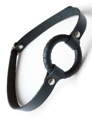 The O-Ring Gag is shown against a blank background. It is a metal O-ring wrapped in a thin strip of black leather attached to a thin, black leather strap.