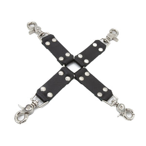 The black Leather Hog Tie is displayed against a blank background. A metal O-ring is in the center with four leather strips attached to it in the shape of an X. Each leather strip has a metal snap hook on the end.