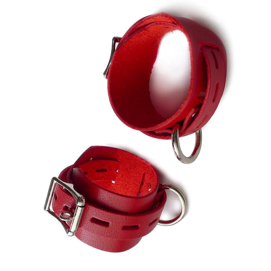 The Locking/Buckling Red Leather Cuffs are shown against a blank background. The cuffs are made of a wide piece of red leather with a narrower, notched piece of leather wrapping around them. Each cuff has a silver D-ring and a lockable buckle.