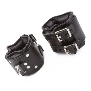 The Premium Lockable Dungeon BDSM Leather Wrist Cuffs are shown against a blank background. They are made of black leather with silver hardware. The cuffs are wide and padded. They have a D-ring and two adjustable straps with lockable buckles.