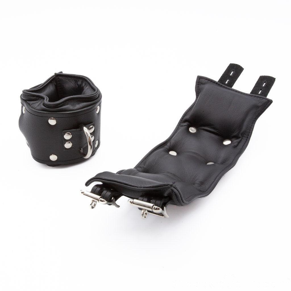 The Premium Lockable Dungeon BDSM Leather Wrist Cuffs are shown against a blank background. They are made of black leather with silver hardware. The cuffs are wide and padded. They have a D-ring and two adjustable straps with lockable buckles.