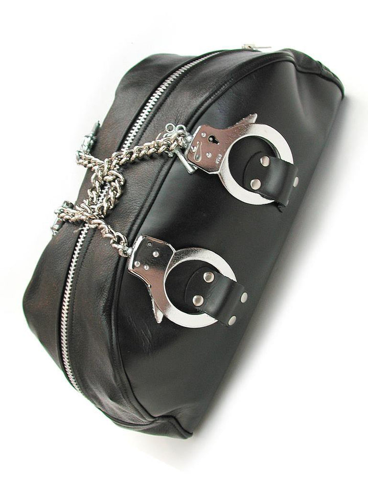 The Leather Doctor Bag with Handcuff Handles is shown against a blank background. It is a black leather bag shaped like a semi-circle. It has a metal zipper on top and chain-link handcuffs as handles.