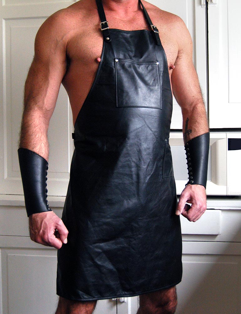 A shirtless muscular man is shown wearing the black Leather Apron, which has adjustable straps and a pocket on the chest. The apron cuts off above the knees. He is also wearing leather arm gauntlets.