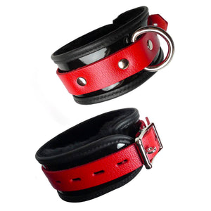 The Firecracker Patent Leather BDSM Ankle Restraints are shown against a blank background. They are made of black patent leather with a thin strip of red leather wrapped around the middle. They have silver hardware.